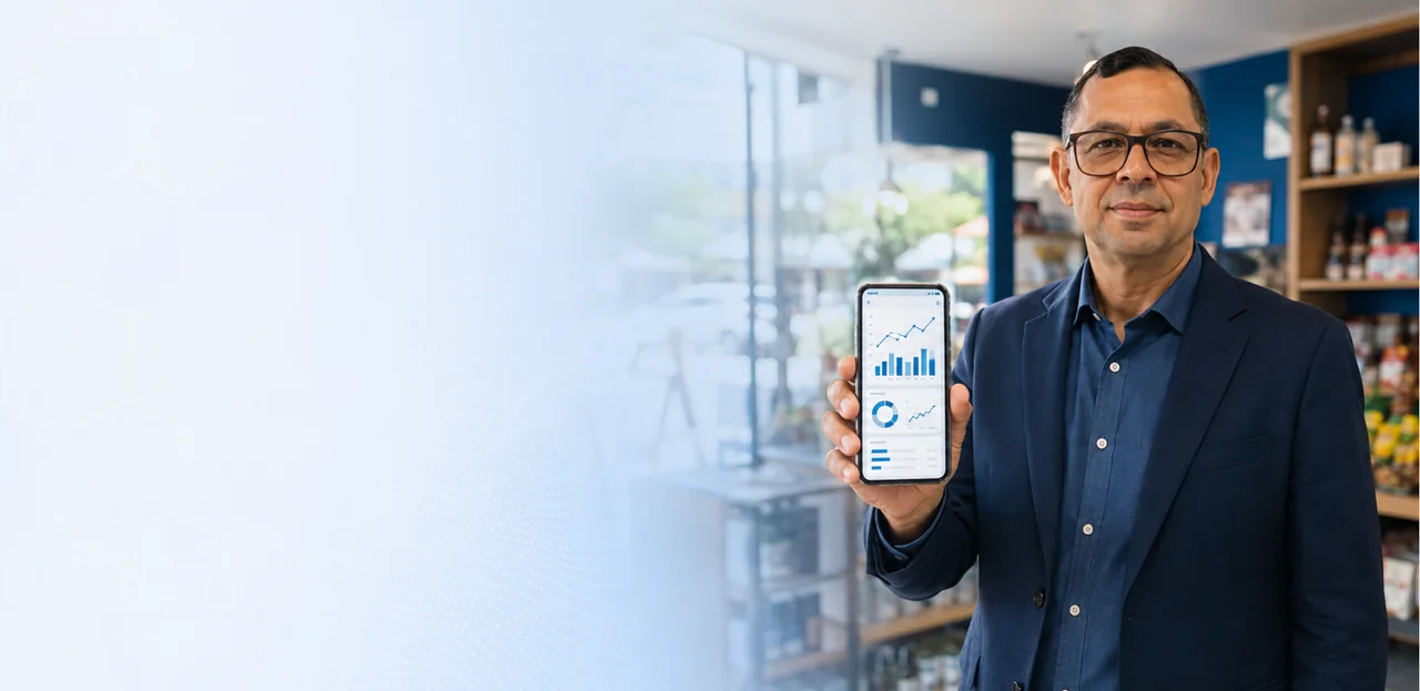 Cláudio Ramos apresenta no celular um painel de gestão digital em um ambiente comercial.